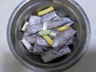 香煎带鱼,把葱段和姜片放在装有带鱼的盆中。