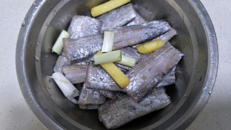 香煎带鱼,把葱段和姜片放在装有带鱼的盆中。