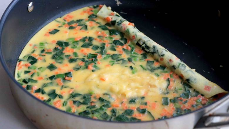 菠菜胡萝卜厚蛋烧,卷起3/1鸡蛋饼，再倒入剩下的蛋液混合物，盖上锅盖，直到表面蛋液混合物凝固8成熟之后；
