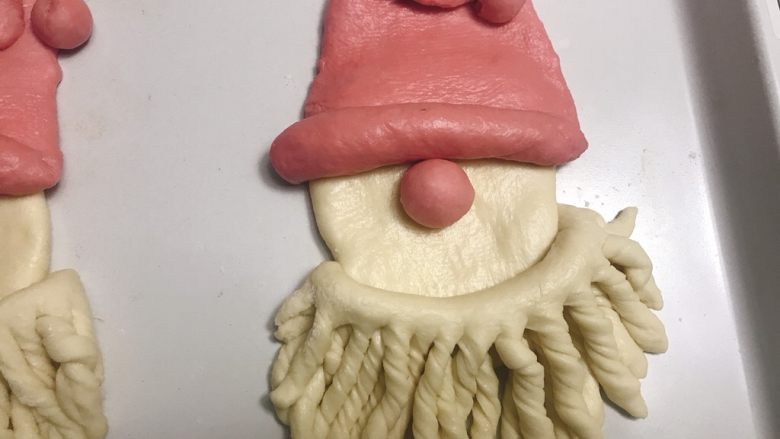 圣诞老人面包,把胡子组装在脸上，每根都扭成螺旋状。再按上红鼻子。
入温暖湿润处进行最后发酵30到40分钟。