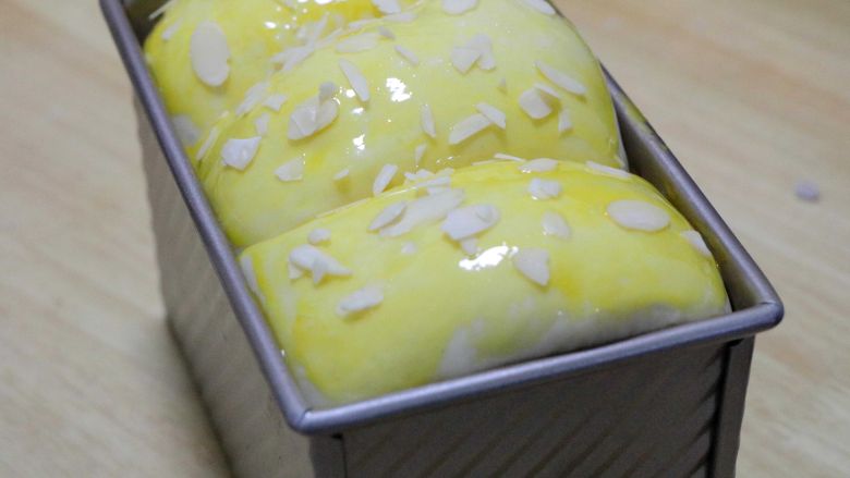 色拉油版吐司,放置温暖的地方发酵至9分满，刷一层蛋液，撒适量的杏仁片