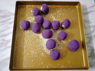 紫薯芝麻饼,烤盘撒适量芝麻，放入紫薯球不停抖动翻滚