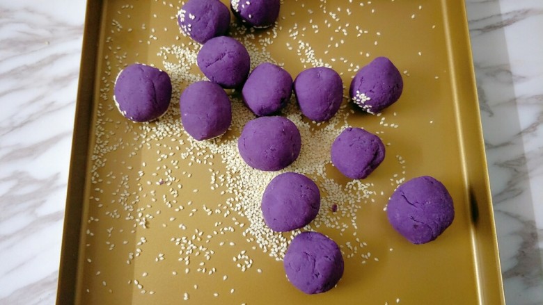 紫薯芝麻饼,烤盘撒适量芝麻，放入紫薯球不停抖动翻滚