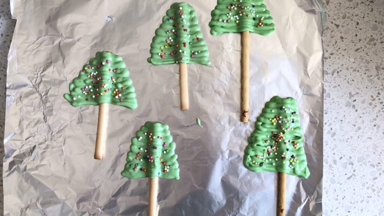 圣诞姜味蛋糕,如图所示把巧克力挤刀饼干棒上，做成圣诞树的样子，撒上彩珠糖，放入冰箱冷藏