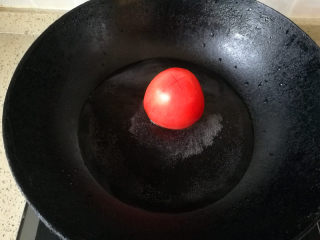 酸甜年糕,取一锅，放少量水，烧开，将西红柿顶部切个十字，放入开水里滚上一圈后捞出，将皮撕掉。