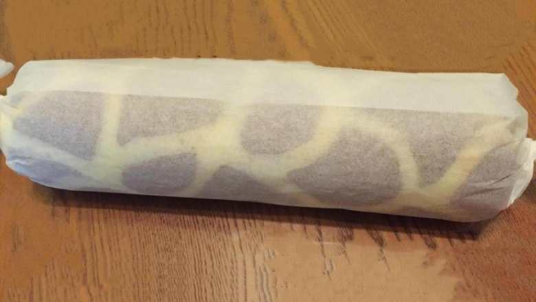  长颈鹿纹蛋糕卷,借助擀面杖用油纸把蛋糕卷卷起来，油纸两边收紧，放冰箱冷藏半小时以上。