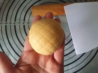 蜜豆菠萝包,提起保鲜膜反扣在左手心，再撕去保鲜膜、用刮板轻轻地划出网格花纹