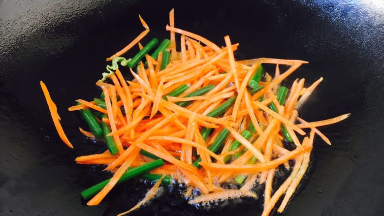 什锦炒米饭,放入胡萝卜丝和蒜苔，煸炒几下，使胡萝卜断生。

