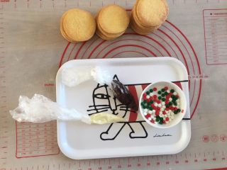 快手圣诞驯鹿饼干,接下来开始装饰的工作了。黑白巧克力都装入裱花袋，隔水融化，在袋子的前端剪一个小口，在饼干上画上驯鹿的犄角和眼睛。