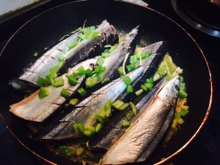 香煎秋刀鱼,将鱼放入锅内，表面再撒一些青椒丁和葱花（鱼有点儿大，切开了😄）