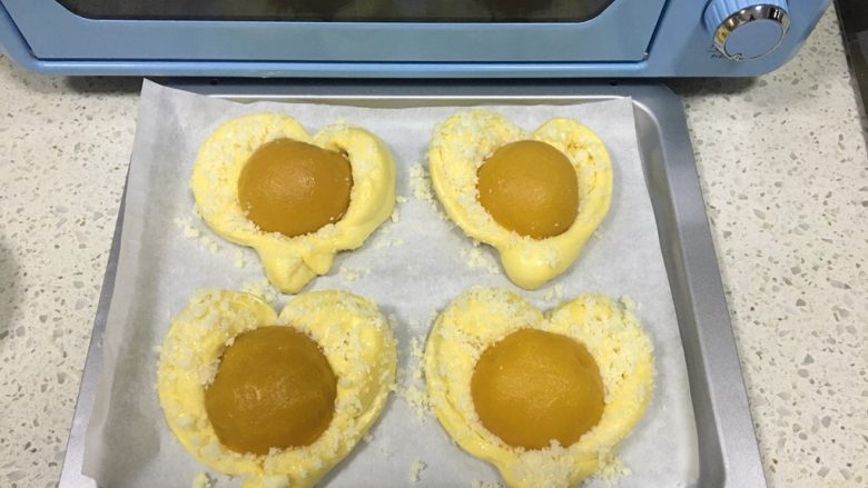 黄桃椰蓉心形面包,发酵后的体积是原来的1.5倍大小，取出发酵好的面团，刷上薄薄一层全蛋液，均匀撒上准备好的黄油椰蓉，把黄桃果肉放在面团中间，往里按压，将黄桃固定住