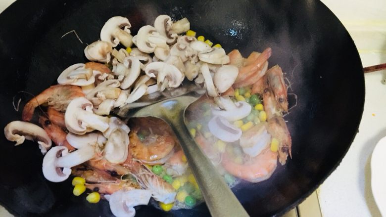 蘑菇海鲜焗饭,先大火炒虾炒熟后放入玉米豌豆转小火最后放入蘑菇。放入盐少许