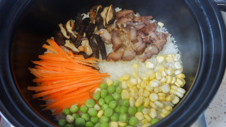 超简单又好吃的彩虹煲仔饭,6、	胡萝卜丝、青豆、玉米粒摆在米饭上，中间留出一个洞