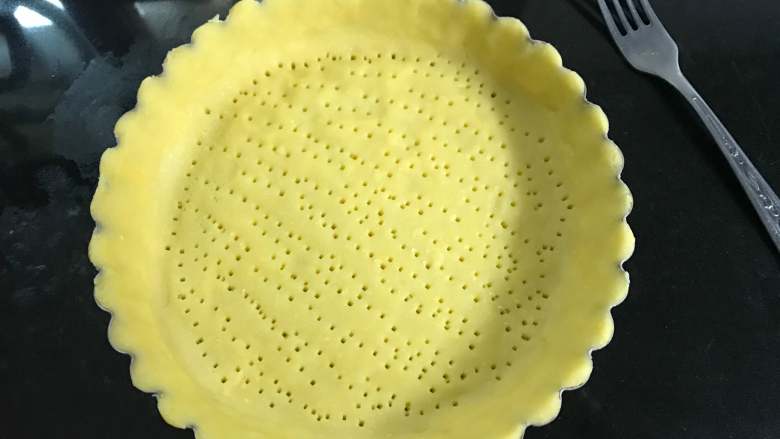 烧果子乳酪挞,30分钟后拿出把面团擀成薄面片放入挞盘中压出形状，用叉子在底部扎一些孔洞。