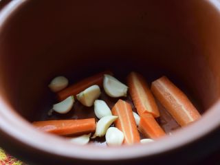 无难度慢炖锅豉油鸡,大蒜和胡萝卜铺在慢炖锅底上。