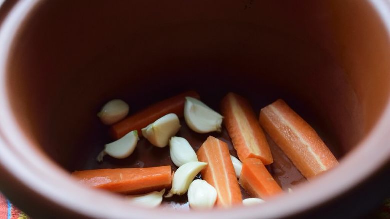 无难度慢炖锅豉油鸡,大蒜和胡萝卜铺在慢炖锅底上。