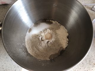 蔓越莓提子黑麦软欧,厨师机面盆内先倒入清水，再倒入高筋面粉和黑麦粉，盐和糖对角线放置，面粉中间挖一小坑放入活性干酵母