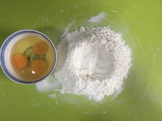葡萄干萨其马,中筋面粉和泡打粉混合均匀，然后倒在揉面垫上，中间挖个坑，准备盛鸡蛋液