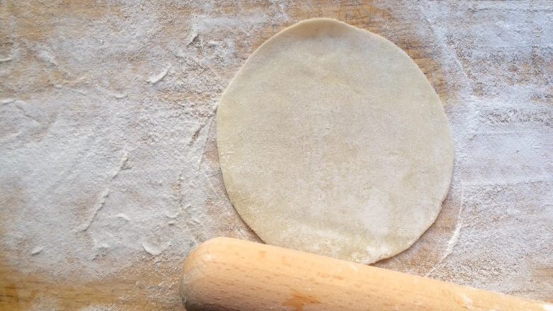 椒香酥脆的饺子皮葱花饼,菜板上撒上少许面粉，饺子皮擀薄