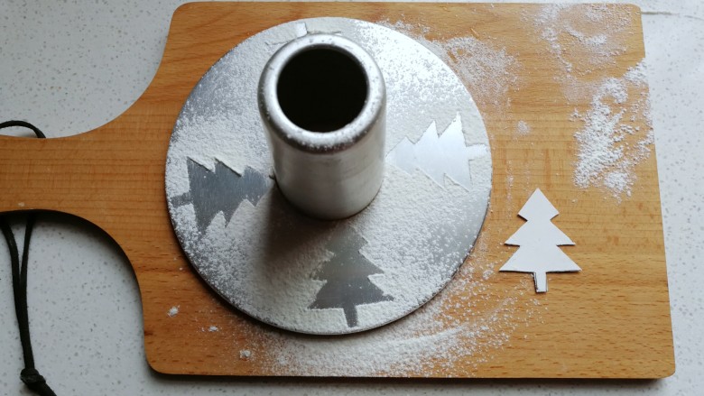 圣诞风双色戚风蛋糕,先做准备工作：用硬纸剪出圣诞树模型，然后摆在中空模具底坐上筛上面粉，移开后就得到圣诞树轮廓了，然后轻轻移置旁边备用；