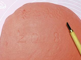 新年快乐,然后取一红色面团擀成1cm厚的面片，用美工刀轻轻地刻写出“2 0 1 8 新 年 快 乐 ”的字样。