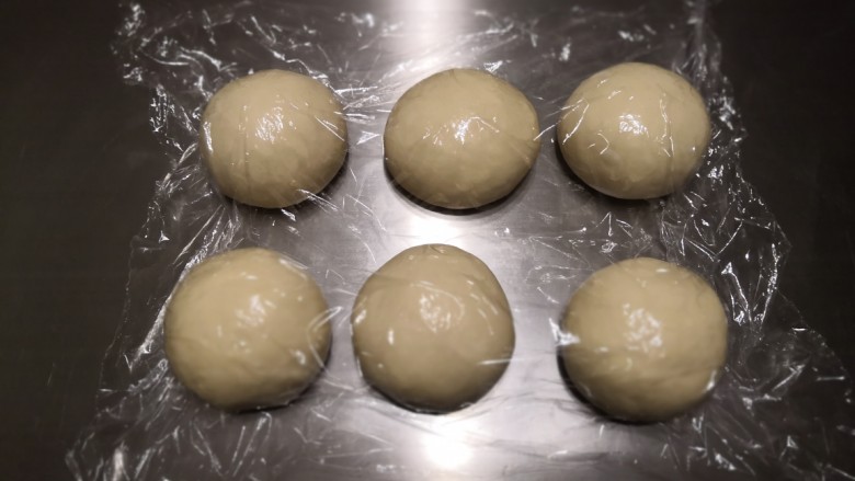 奶香辫子面包,将面团排气后分割成6份滚圆，盖上保鲜膜松弛15分钟。