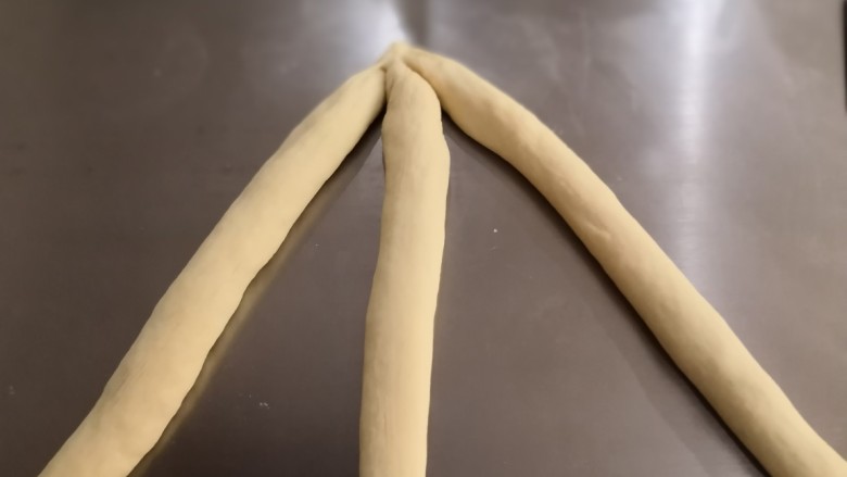 奶香辫子面包,取三根长条将它们的一端重叠在一起压紧。