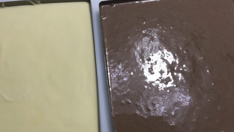简单制作两款彩绘蛋糕卷~UKOEO 风炉制作,取出油布，放入两个28厘米的烤盘，各倒入面糊，别忘了可可花纹配原味面糊，原味花纹配可可面糊。