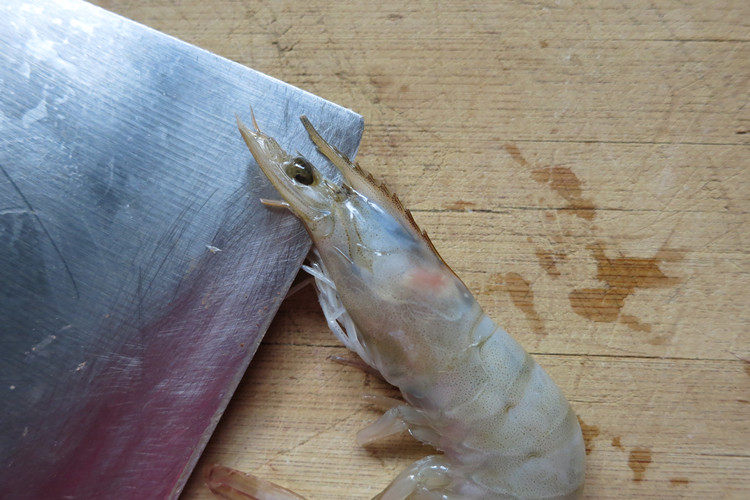 翘尾巴的金银蒜蓉开背虾,虾平铺在板上，一手按住虾身，刀从虾头的两眼之间入刀