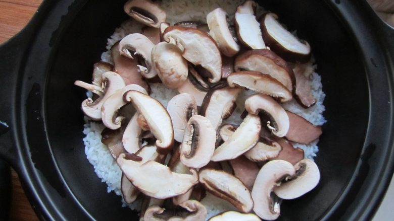 腊肉煲仔饭,蜂鸣声响起时把香菇、口蘑片铺在表面，在锅四周淋入一勺食用油，加盖再次启动按钮