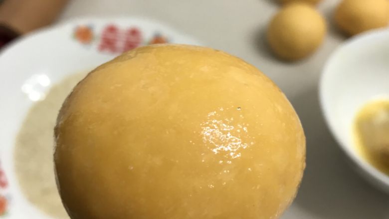 南瓜花环面包,取一个面团，用手捏住底部表面刷上全蛋液。