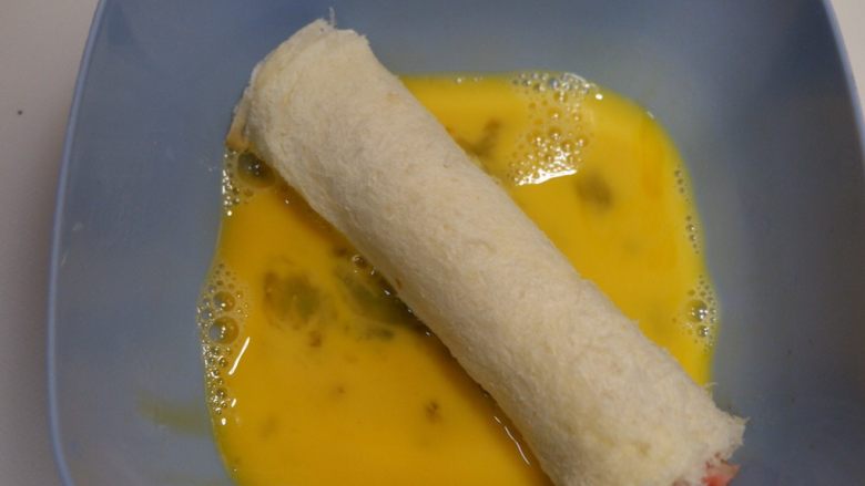 快手早餐—香肠吐司卷,将吐司卷放在蛋液里，均匀的裹粘上鸡蛋液