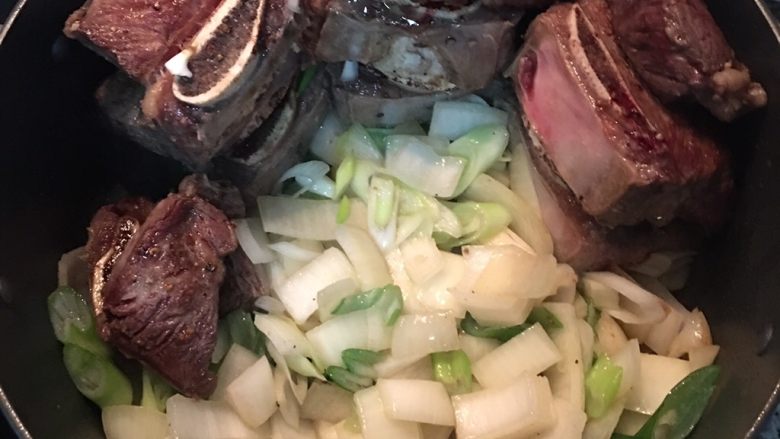 日式炖牛小排,将煎上色的牛小排延锅边堆起来，腾出空间放入大葱与洋葱炒香；