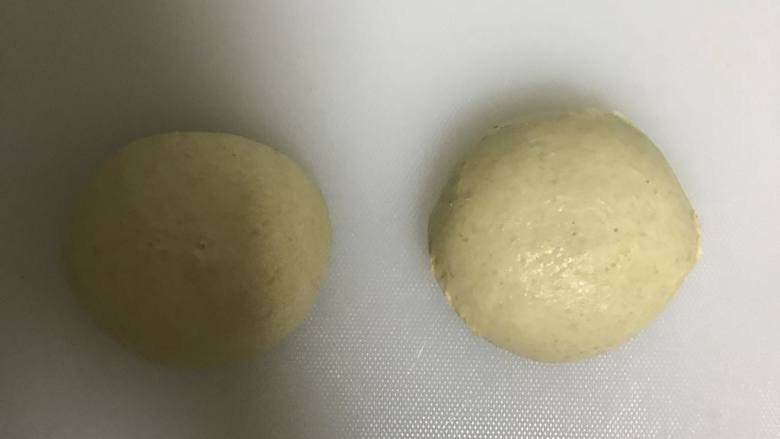 全麦豆沙麻薯肉松软欧面包,取出按压排气，平均分成2份滚圆，盖上保鲜膜松弛10分钟。