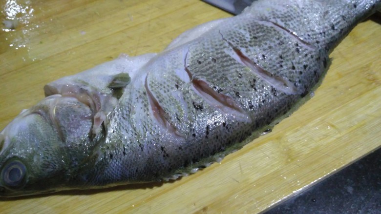 柠檬烤鲈鱼,鱼身切几刀，鱼肚子切开，一会儿要把鱼爬在烤盘上，把盐抹在身上，腌半个小时