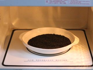 花生芝麻牛轧糖,把黑芝麻放入微波炉加热约1分30秒至熟。