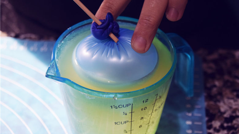 吉丁水晶球—可以吃的水晶球,将我们只做的气球模具，进入到吉利丁液中，此时吉利丁液应该低于手温。按压不下去的时候可以用另一只手帮助按压。