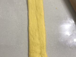 胡萝卜奶香吐司,用擀面杖从中间向俩头擀开，整理成差不多宽厚，长在30厘米宽在7厘米左右的长舌形，靠近自己的一方用手压扁。
