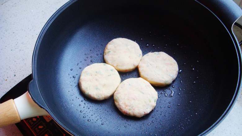 香葱土豆饼,炒锅里倒入少许食用油，饼胚在手掌里按扁放入锅中。