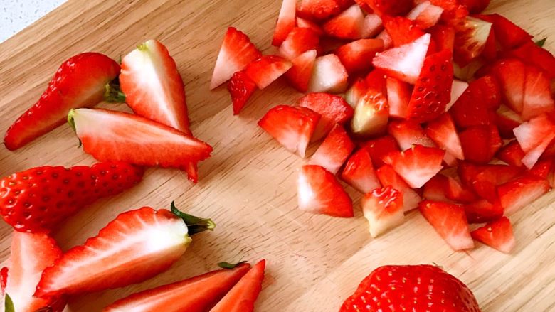 草莓奶油瑞士蛋糕卷,草莓切一些丁,再切几瓣带叶子的草莓瓣,用来做表面装饰。