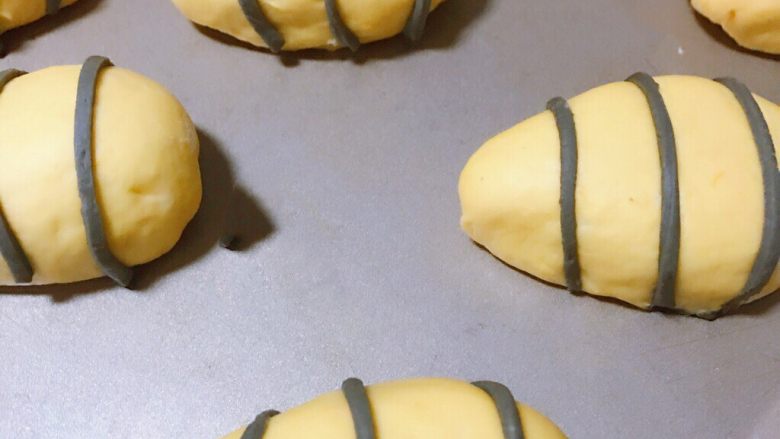 肥美小蜜蜂椰蓉包,将黑色细条均匀裹在黄色椭圆形面团上，每个面团裹三条
