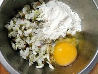 做饼+槐花塌子,将洗净的槐花沥水后放进容器，打入1个鸡蛋，加入适量面粉和少量的盐。