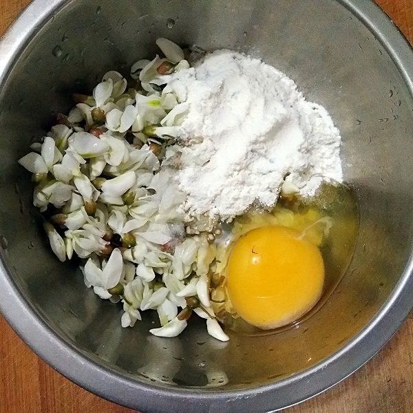 做饼+槐花塌子,将洗净的槐花沥水后放进容器，打入1个鸡蛋，加入适量面粉和少量的盐。