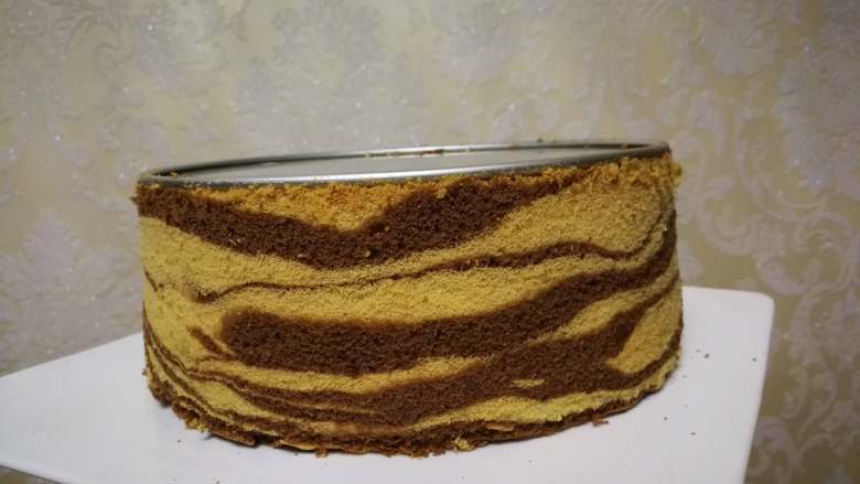 斑马纹戚风蛋糕,脱模可以用手轻轻掰蛋糕一圈，使其慢慢与模具分离，然后轻轻推底部，或直接用脱模刀划一圈，再推模具底部。用锯刀反面轻轻把底部脱下来
