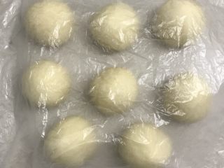 椰蓉花朵面包,取一个面团光滑面在上，分割下来的小块压里面滚圆盖上保鲜膜松弛15分钟。