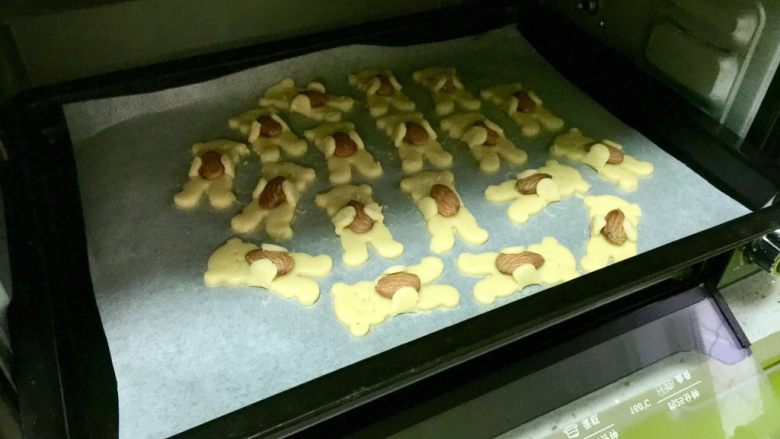 小熊扁桃仁饼干,把油纸连同饼干一起移入烤盘，烤箱预热175度，放入中层，上下火烤10～12分钟。注意观察不要上色过度。