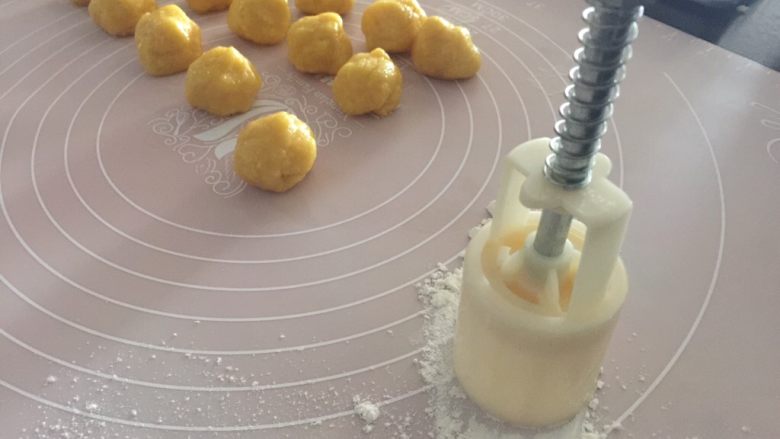 椰蓉桃酥,桌面撒些面粉，50克规格的小月饼模先在面粉上按压一下粘些粉防粘