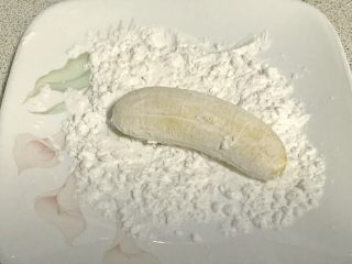 百变水果+酥炸香蕉,拿一个香蕉蘸上干淀粉，拍掉多余干粉。