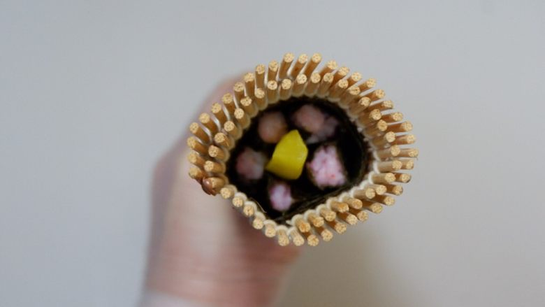 樱花寿司,用寿司帘卷成圆筒形。从开口处看一下。里面是否已经形成了樱花的形状。如果OK了~就在海苔边缘抹少许沙拉酱粘合，多余的海苔剪掉。做好放一旁备用。