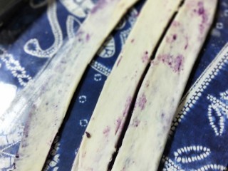 紫薯辫子面包,将长方形的面团向长条形方向擀长擀薄，紫薯如果漏出来也无妨。用刮板将面皮分成3长条。